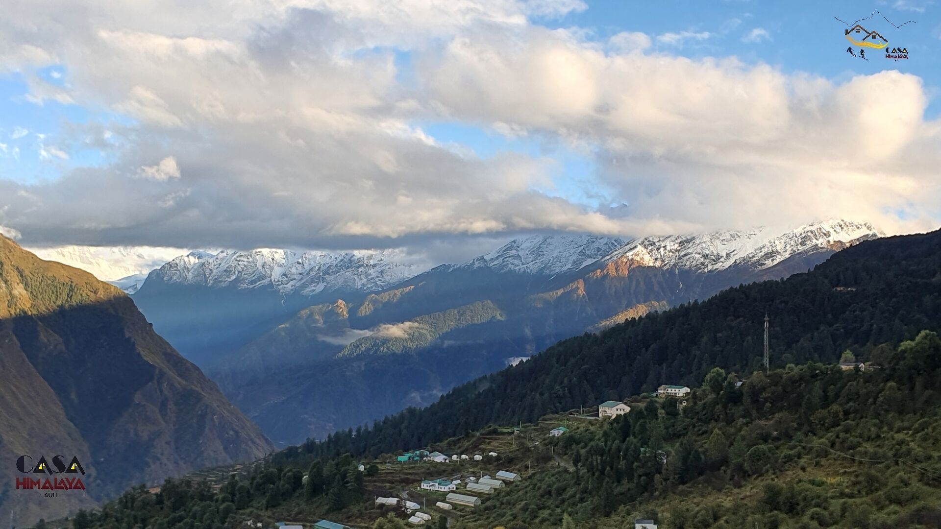 A mountainous landscape with snow-capped peaks, a valley with scattered houses, and a clear sky.