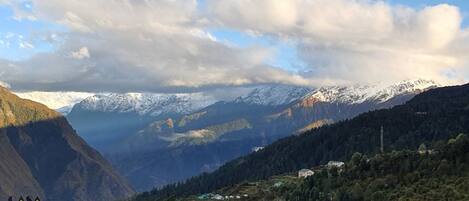 A mountainous landscape with snow-capped peaks, a valley with scattered houses, and a clear sky.