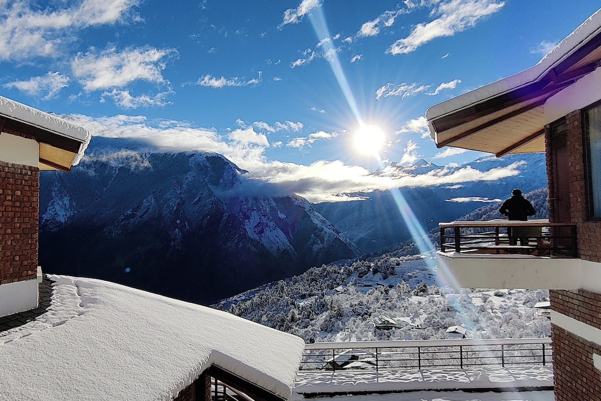 Un balcón cubierto de nieve con vistas a la montaña, un edificio de ladrillo y una persona de pie en el balcón.