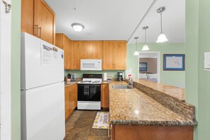 A kitchen with wooden cabinets, a white refrigerator, a microwave, a stove, and granite countertops.