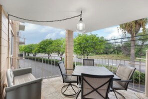 Een balkon met een tafel en stoelen, met uitzicht op een straat en groen.