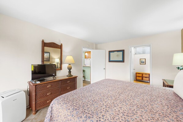 A bedroom with a bed, a dresser, a television, a mirror, and a door leading to a bathroom.