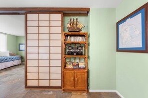 A room with a sliding shoji screen, a bookshelf with books and audio equipment, a bed with patterned bedding, and a map on the wall.