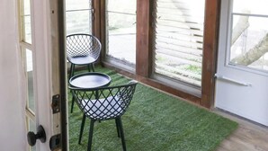 Una stanza con soffitto in legno, due sedie nere dal design essenziale, un tavolino e una porta che dà sull'esterno.