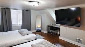 Una camera da letto con due letti, una scrivania, una sedia, una TV, uno specchio e una finestra con tende.