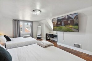 Two single beds with white linens and gray pillows, a flat-screen TV, and a small desk with a chair.