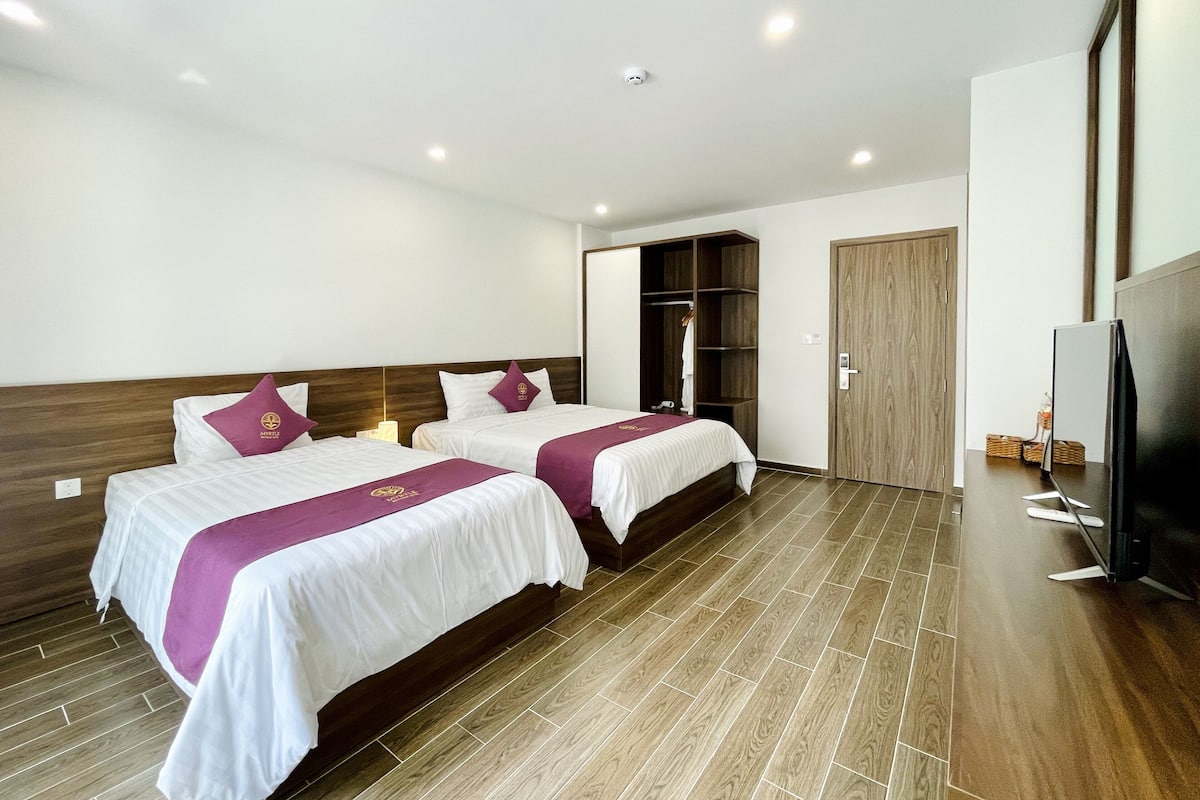 A hotel room with two beds, a wardrobe, a television, and a wooden floor.