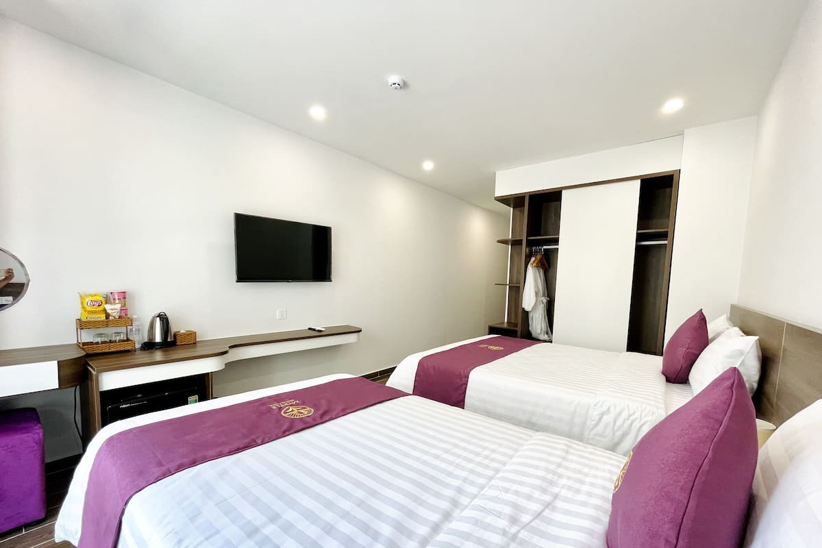 A hotel room with two beds, a TV mounted on the wall, a desk with a kettle, and a wardrobe.