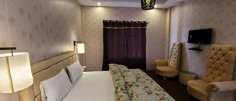 A hotel room with a bed, two armchairs, a TV, and a lamp.