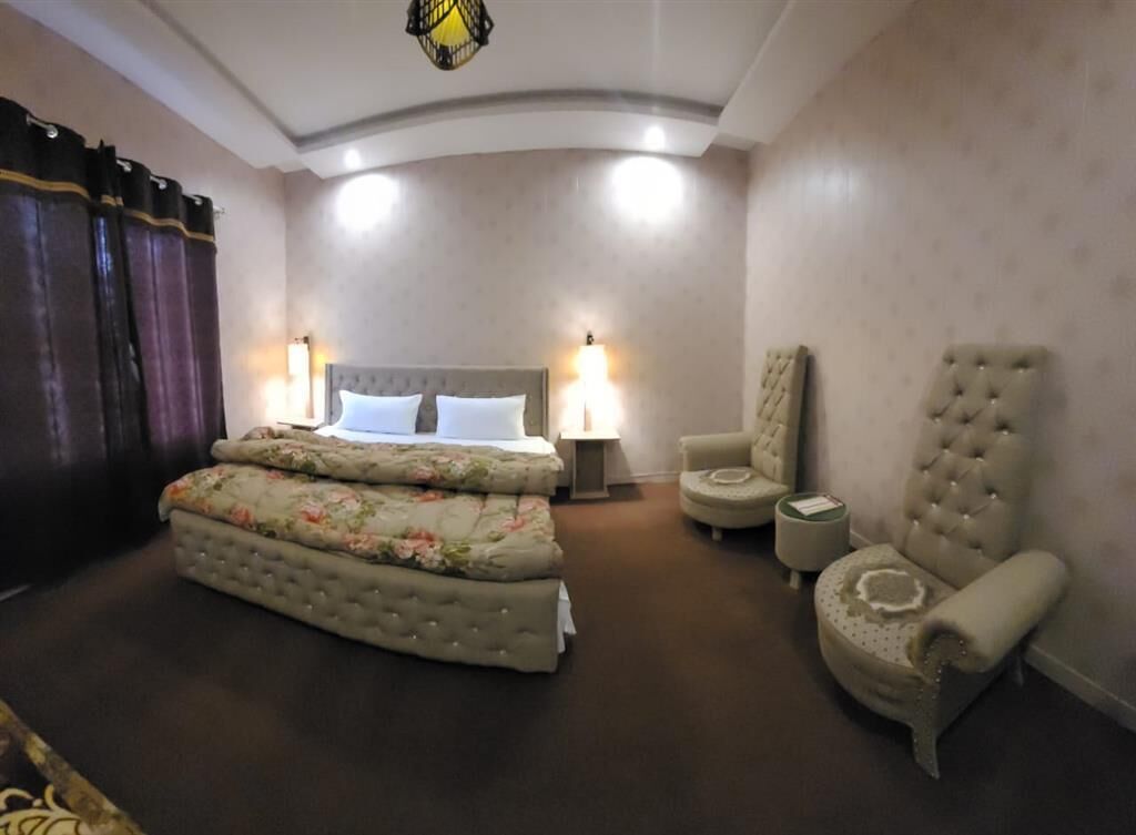 Une chambre à coucher avec un lit double, deux fauteuils, une table de chevet et une lampe.