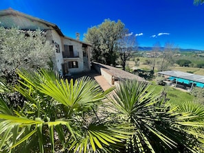 Uma casa de pedra com varanda, cercada por vegetação exuberante e um céu azul límpido.