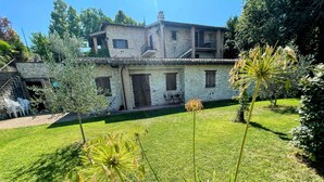 A stone house with a tiled roof, surrounded by a well-maintained lawn and various plants. - Apt 5 Aircon, Wifi, Infinity Pool, Jacuzzi, Gardens Incredible! Sleeps 4 (Spoleto)
