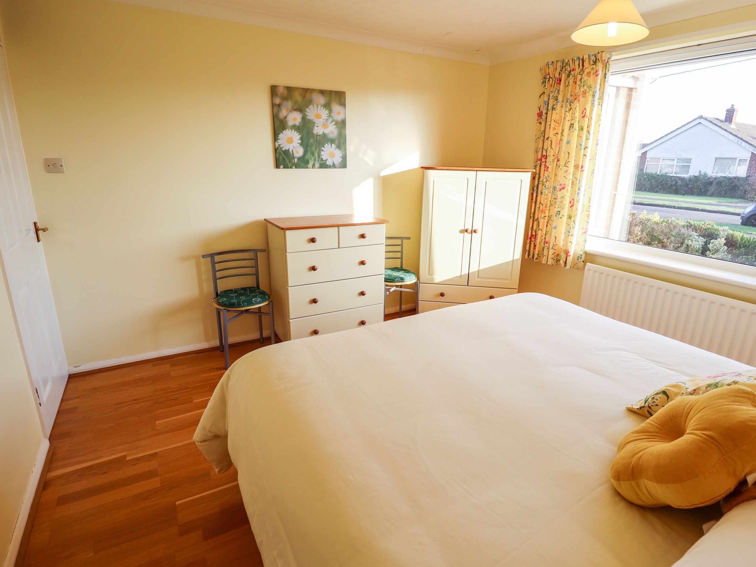 A bedroom with a bed, a dresser, a chair, a window with curtains, and a painting on the wall.