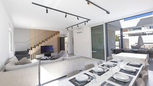 A modern interior with a dining area, sofa, TV, and staircase.