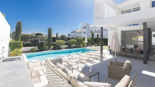 A modern outdoor pool area with lounge chairs, a dining area, and a view of the surrounding landscape.