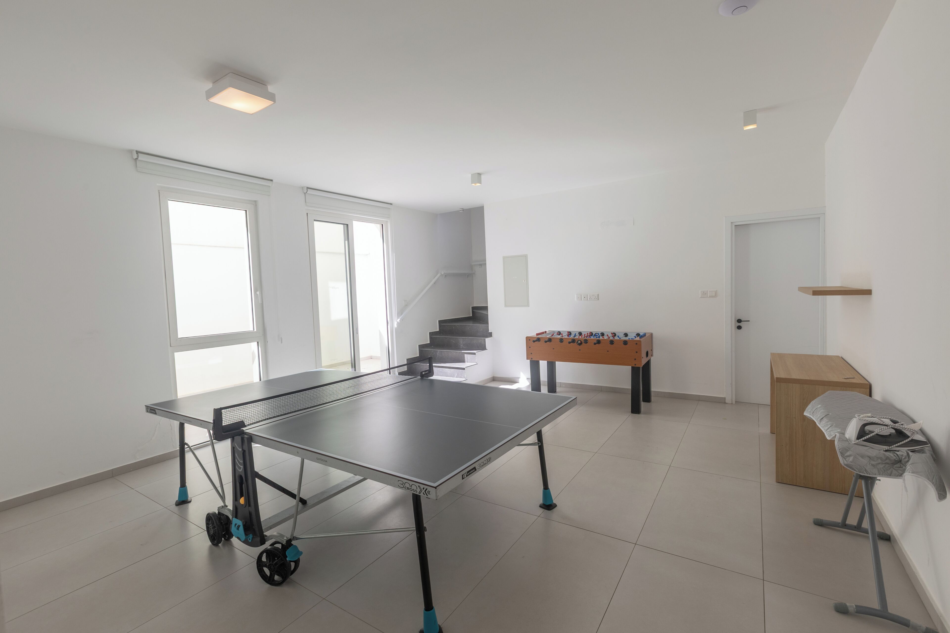 A spacious room with a ping pong table, a foosball table, and a staircase leading to an upper level.