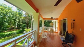 A balcony with white chairs, a ceiling fan, and a view of a garden. - Las Brisas, Juan Dolio, 3br, 2 Pools, Jacuzzi, Beach, Golf, 7 Sleeps (Guayacanes)