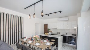 Eine moderne Küche mit weißen Schränken, ein Essbereich mit einem Marmortisch und ein graues Sofa.