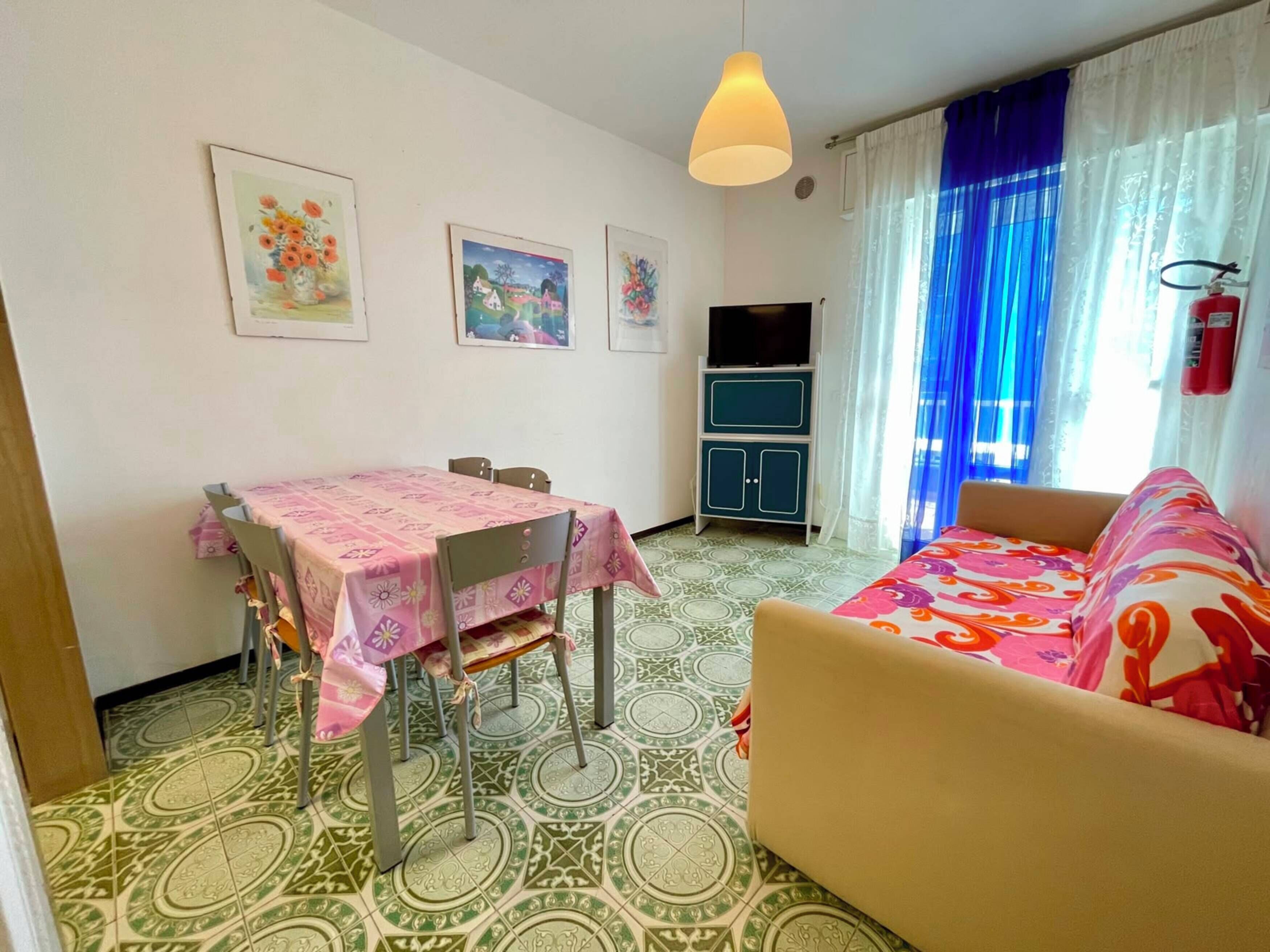A room with a dining table, chairs, a sofa, a television, and a fire extinguisher.