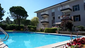 A swimming pool surrounded by a landscaped garden, with a multi-story building featuring balconies and air conditioning units.