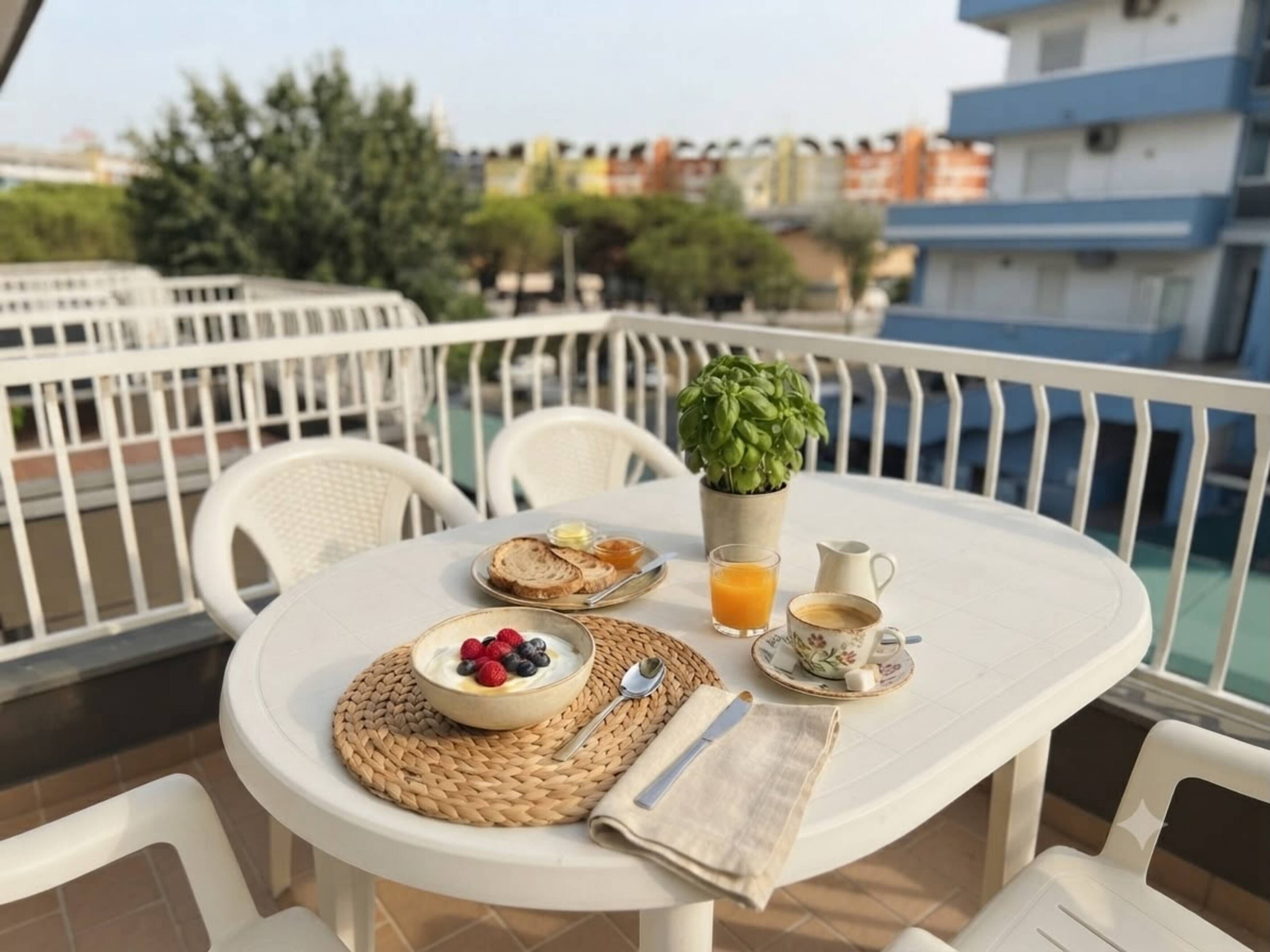 A round table with a breakfast setting on a balcony, including a bowl of yogurt with berries, toast, a glass of orange juice, and a cup of coffee.