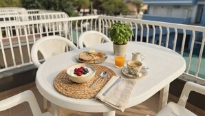 A round table with a breakfast setting on a balcony, including a bowl of yogurt with berries, toast, a glass of orange juice, and a cup of coffee.