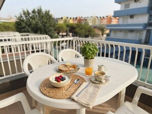 A round table with a breakfast setting on a balcony, including a bowl of yogurt with berries, toast, a glass of orange juice, and a cup of coffee.