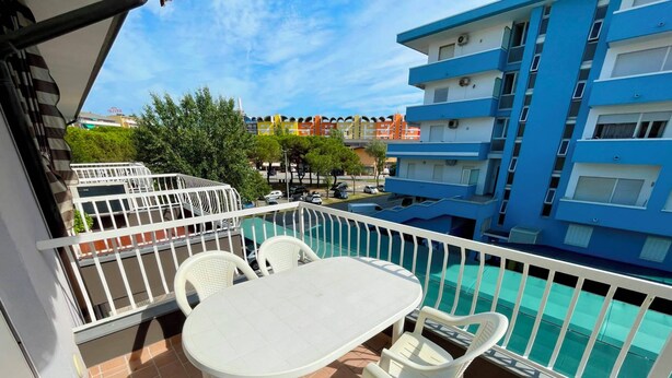 A balcony with a table and chairs, a pool, and a view of a blue building.