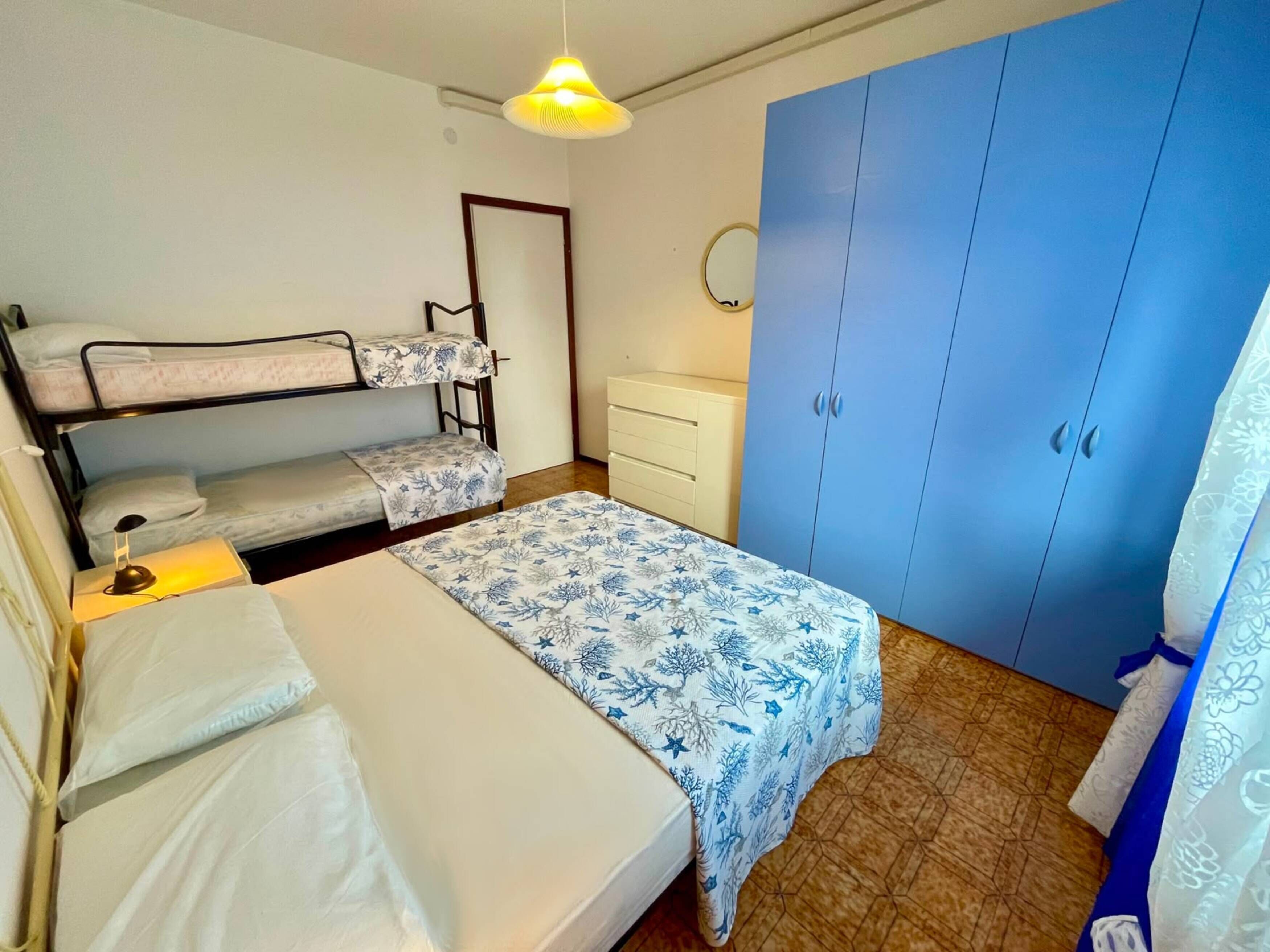 A room with bunk beds, a desk, a wardrobe, and a hanging light fixture.