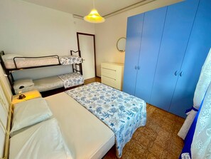 A room with bunk beds, a desk, a wardrobe, and a hanging light fixture.