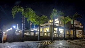 A multi-story building with balconies, a gated entrance, and palm trees.