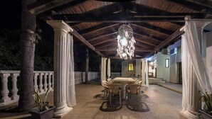 An outdoor covered patio with a dining table and chairs, columns, and a hanging dreamcatcher.