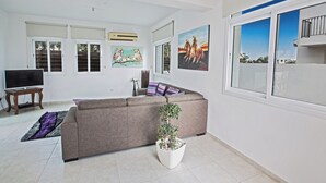 A living room with a sofa, a TV, a potted plant, and artwork on the walls. - Protaras Holiday Villa Me25 (Paralimni)