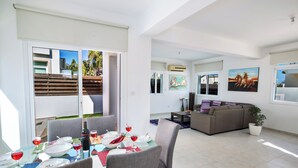 A modern living space with a dining area, a sofa, and a painting on the wall. - Protaras Holiday Villa Me25 (Paralimni)