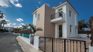 A two-story house with a balcony, a gated driveway, and a clear blue sky. - Protaras Holiday Villa Me25 (Paralimni)