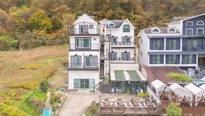 A multi-story hotel with a central staircase, outdoor seating area, and a view of a hillside. - Gangchon Beautiful pet House Pension (Chuncheon)