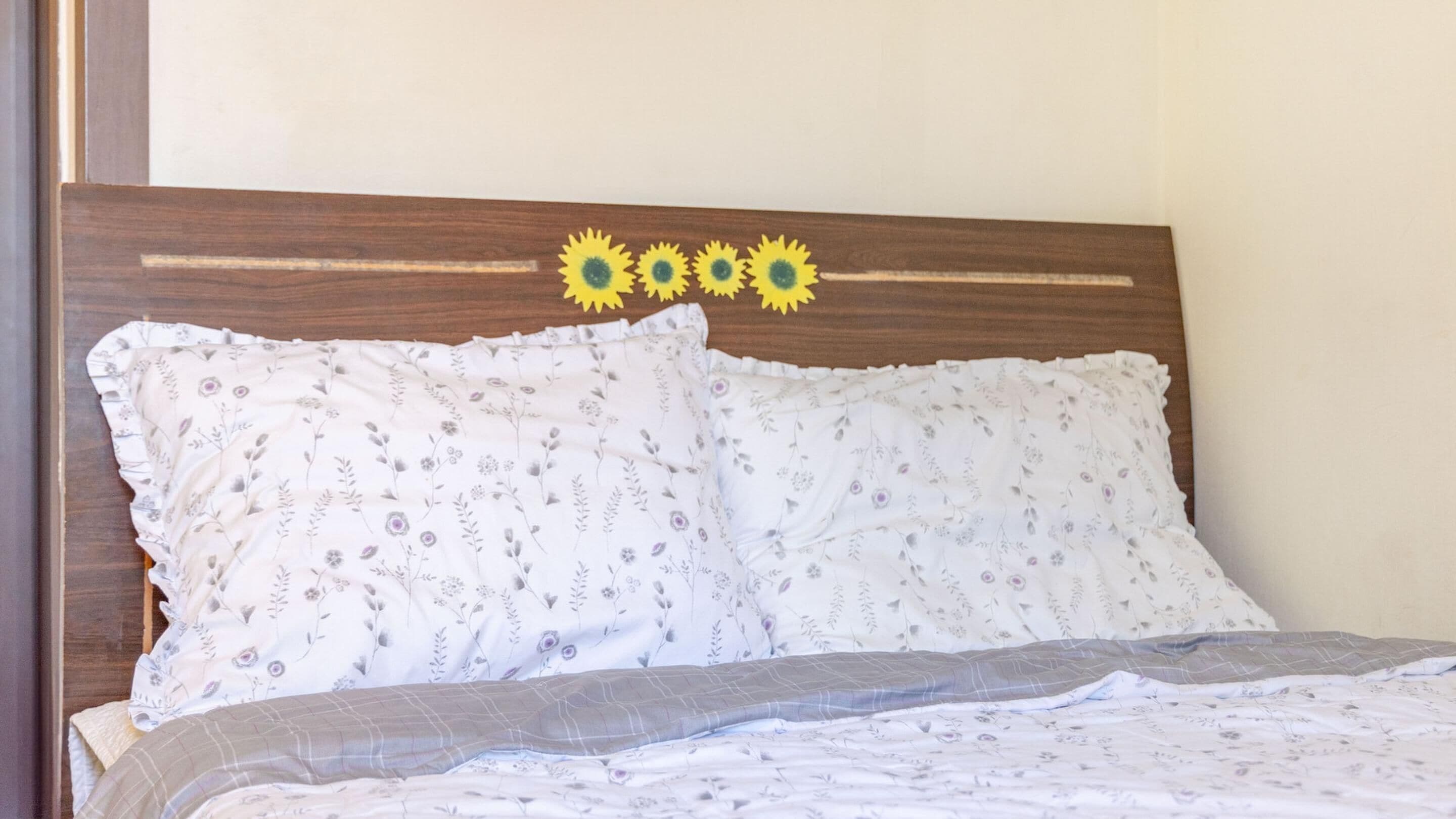 Ein Bett mit Kissen in Blumenmuster und ein Holzkopfteil mit Sonnenblumenverzierungen.