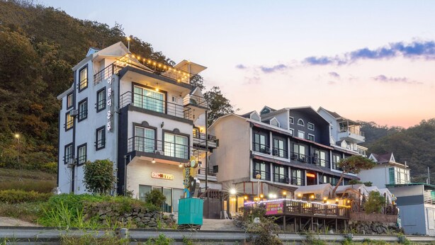 A multi-story hotel with balconies, a restaurant on the ground floor, and a view of the surrounding hills. - Gangchon Beautiful pet House Pension (Chuncheon)