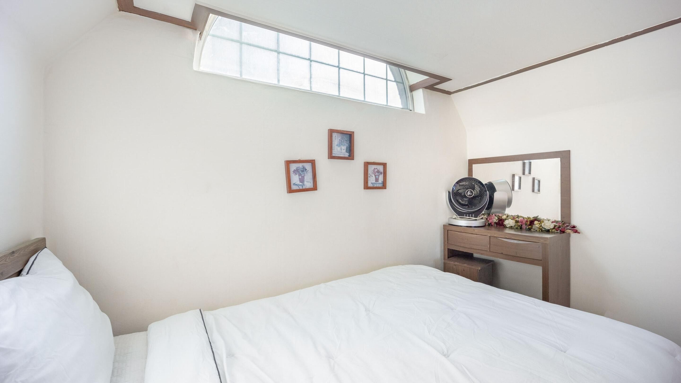 A bedroom with a bed, a desk with a mirror, and three framed pictures on the wall.
