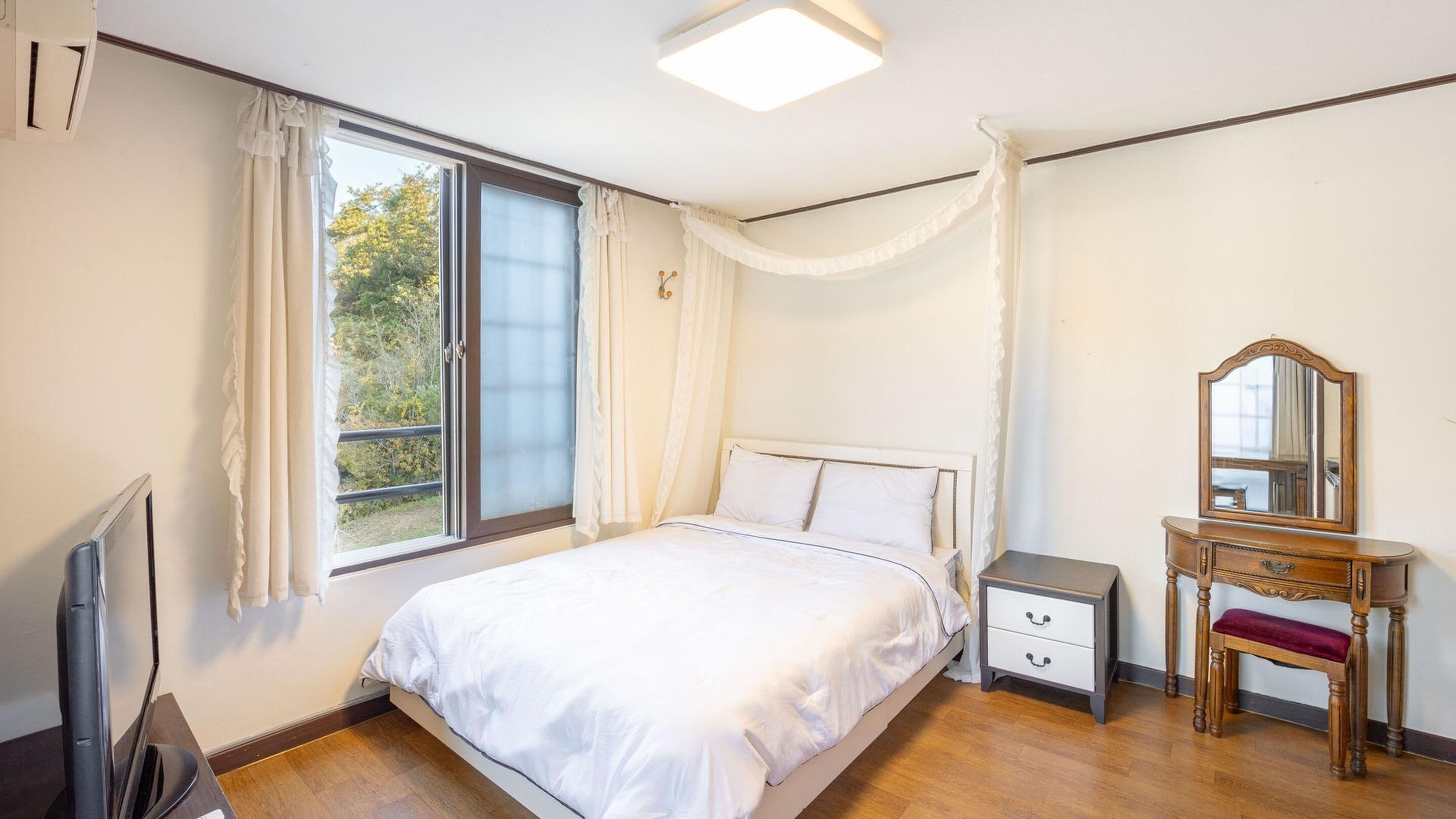 A bedroom with a bed, bedside table, dresser, mirror, and a window with curtains.