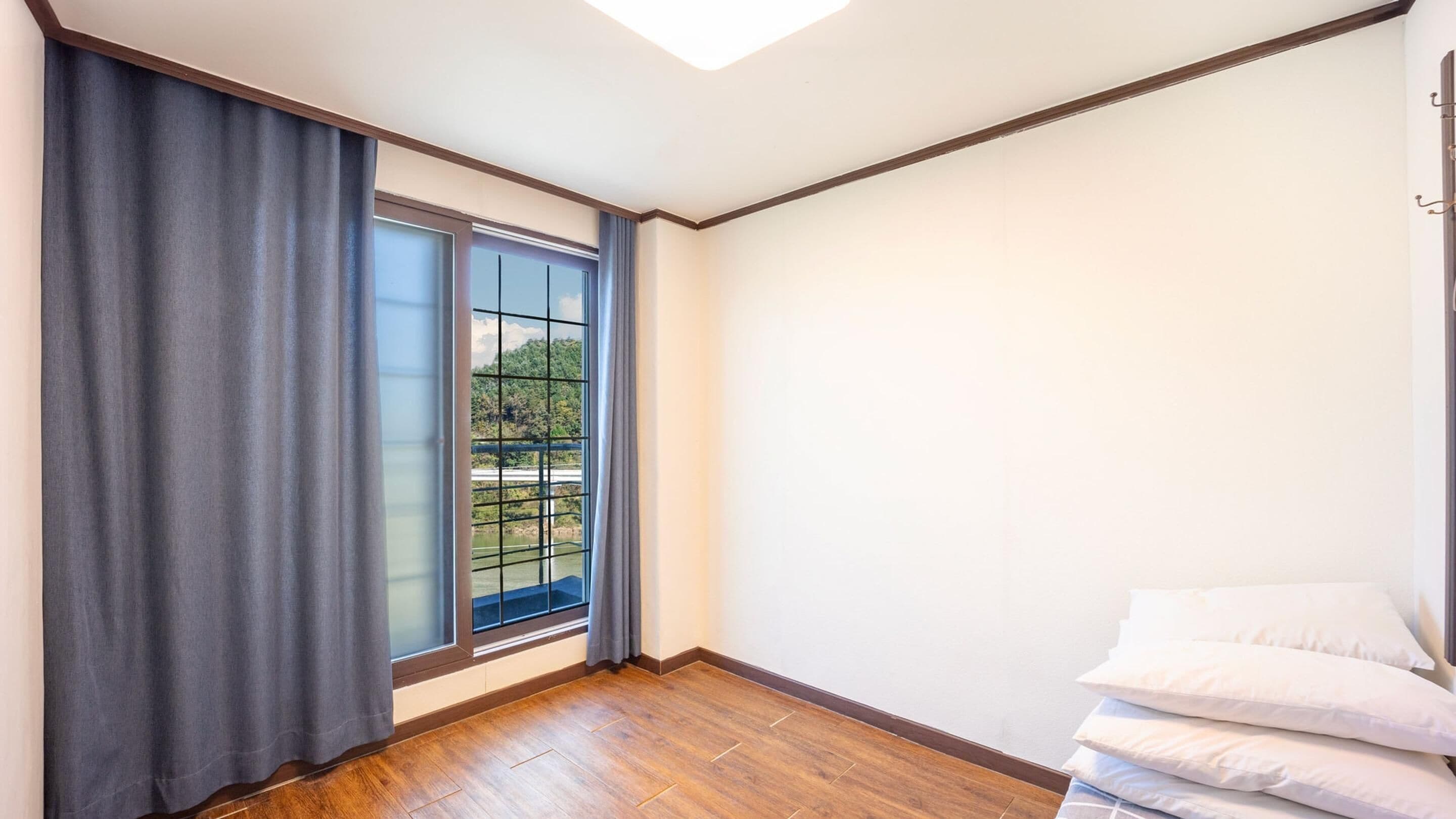A room with a large window, wooden flooring, and a stack of pillows.