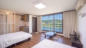 A hotel room with two beds, a small kitchenette, a large window with a view of a bridge and greenery, and a ceiling light. - Gangchon Beautiful pet House Pension (Chuncheon)