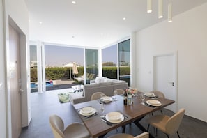 A modern dining area with a table set for four, large windows, and a view of a swimming pool and greenery.