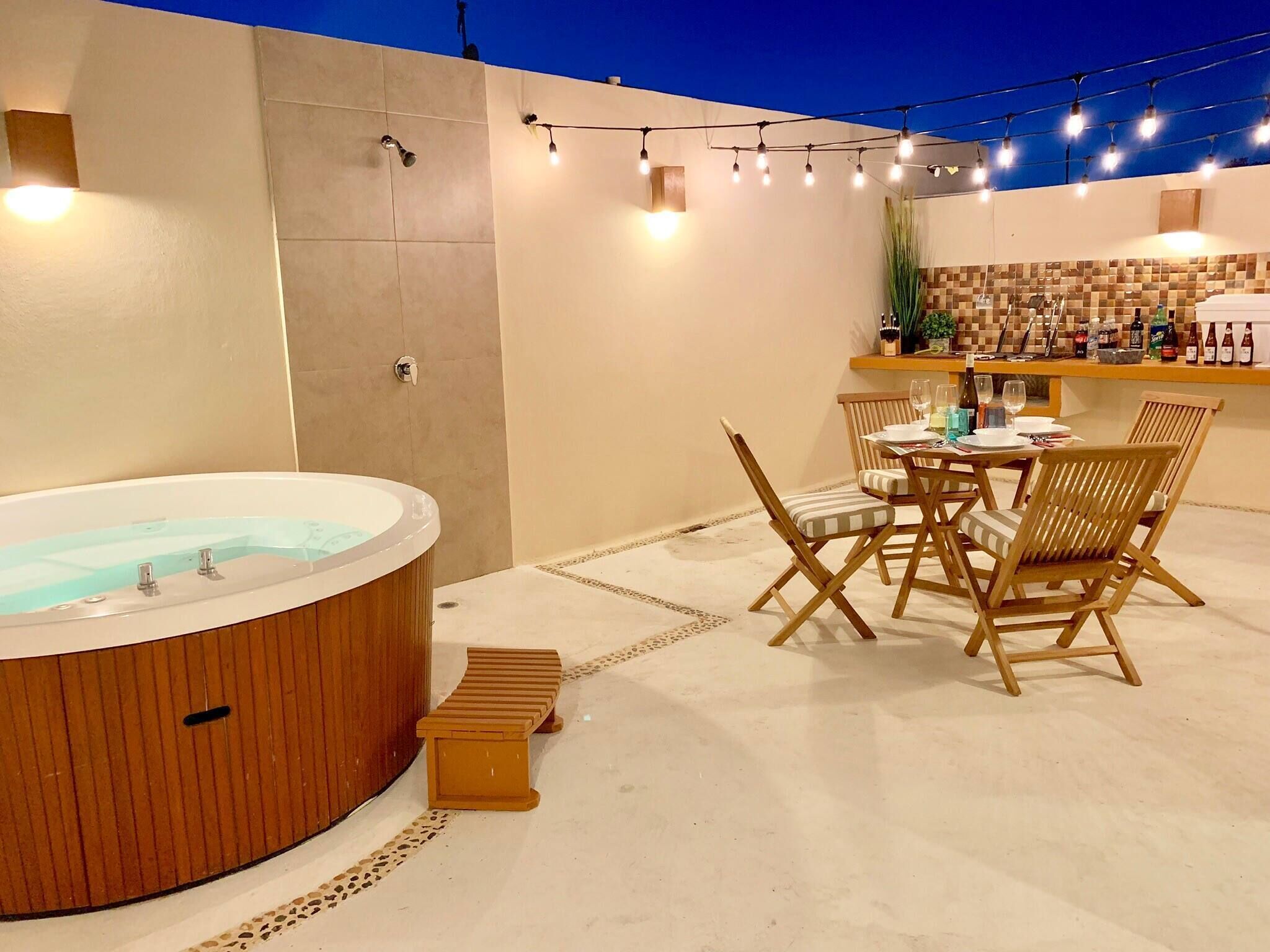 A hot tub with wooden seating, a table with chairs, and a bar area with bottles and glasses.