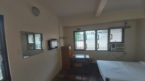 Une petite chambre d’hôtel, composée d’une seule pièce, avec un lit, un bureau et une fenêtre grillagée.