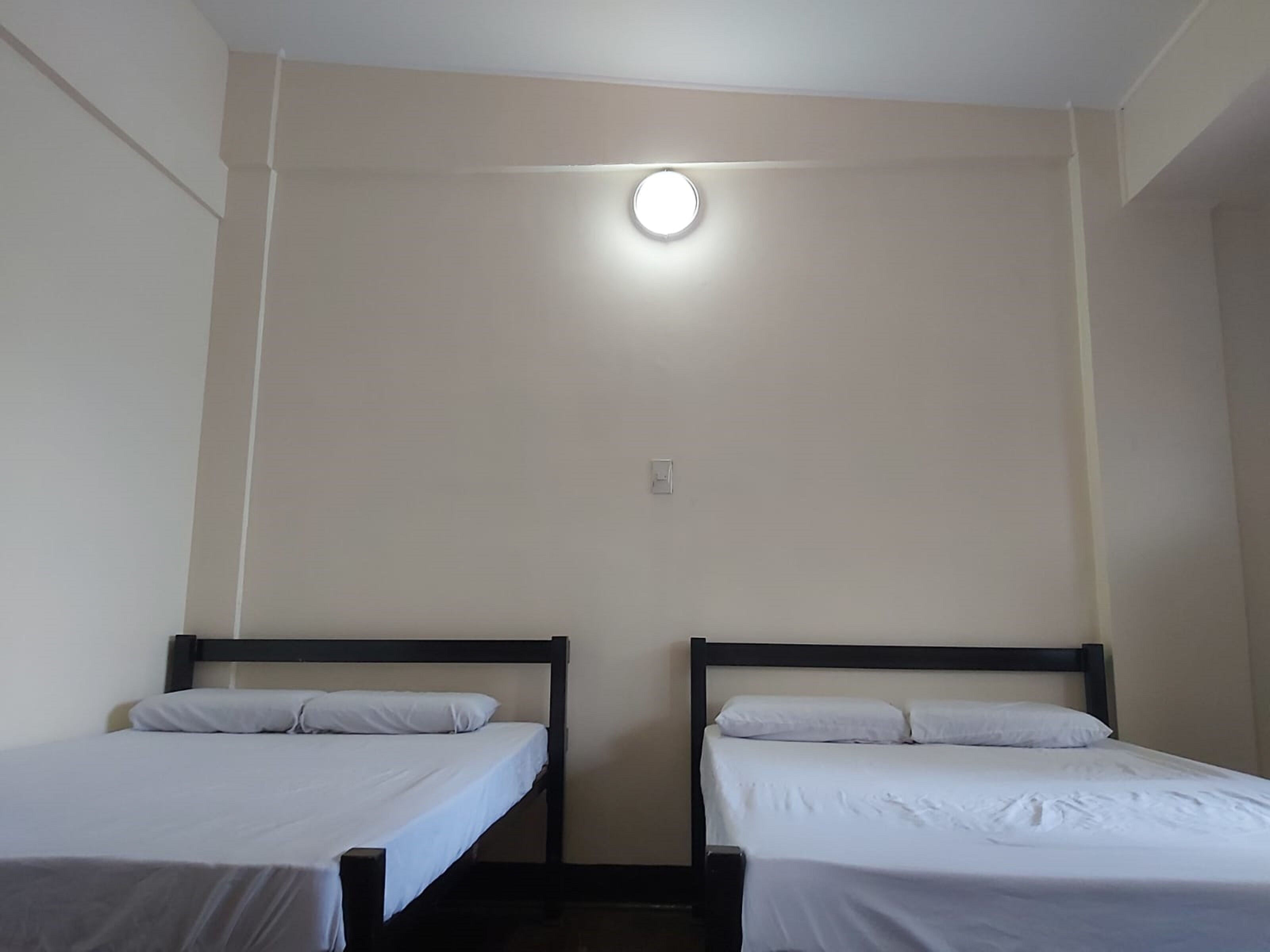 A room with two single beds, a light fixture on the ceiling, and a wall switch.