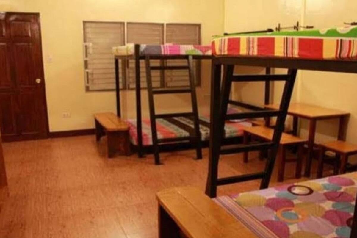 A dormitory room with bunk beds, a small desk, and a chair.