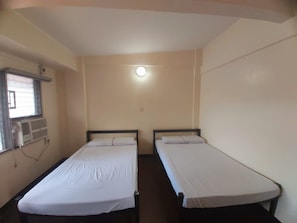 A room with two single beds, a window with an air conditioning unit, and a light fixture on the ceiling. - OYO 916 Angel's Boardrooms (Quezon City)