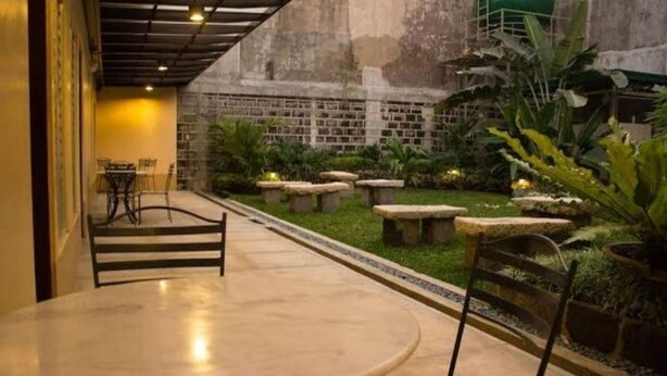 Une cour avec une table ronde et des chaises, des bancs en pierre et des plantes en pot.