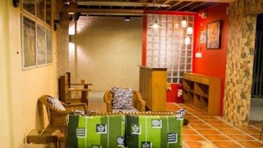 Un salon chaleureux avec un canapé, des fauteuils et une petite table. Une fenêtre offre une vue sur l’extérieur, et un mur rouge présente une texture qui rappelle la pierre.